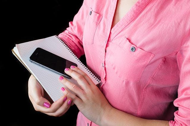 Nő kezében egy füzet és egy telefon, rajta cikluskövető applikációval